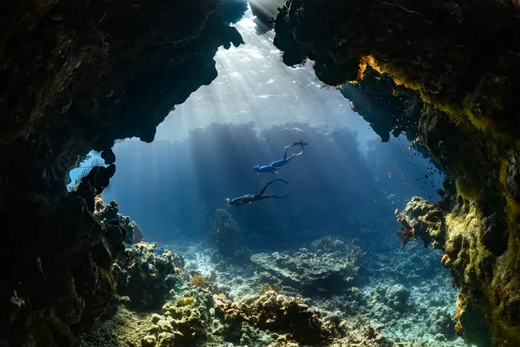 Mergulhadores em uma gruta submarina iluminada pelo sol