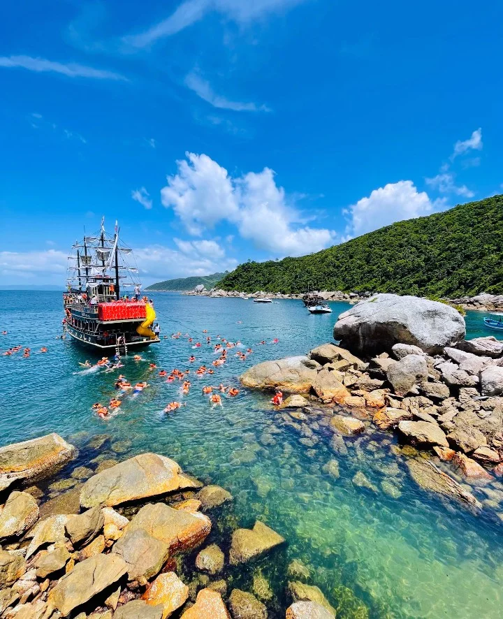 Barco pirata ancorado numa enseada com os passageiros nadando de colete